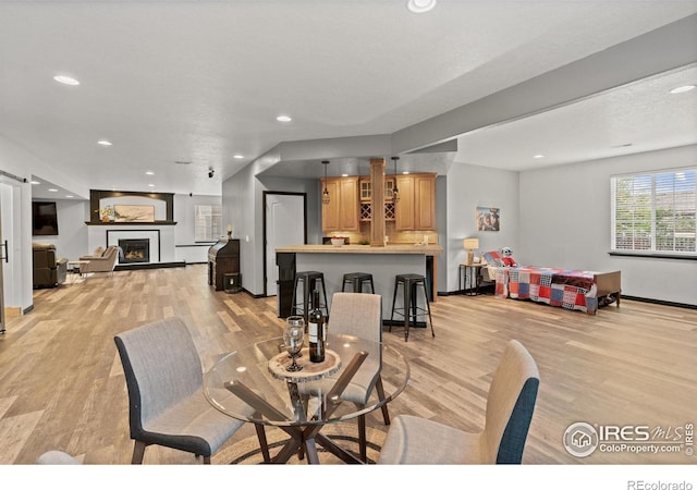 dining area with light wood-style flooring, recessed lighting, a warm lit fireplace, and baseboards