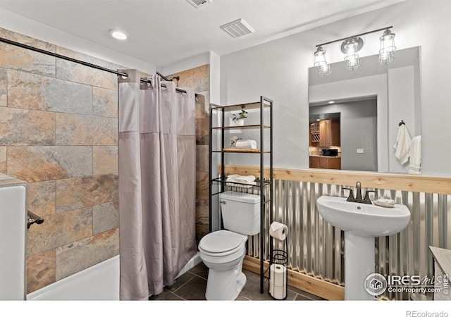 full bathroom featuring a tile shower, toilet, a sink, and tile patterned floors