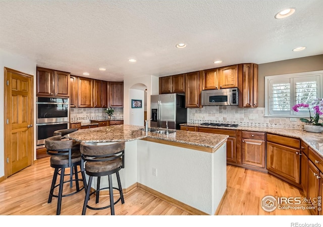 14180 Whitney Cir, Broomfield, CO 80023 - kitchen with appliances with stainless steel finishes, a center island with sink, a textured ceiling, light wood-style flooring, and backsplash