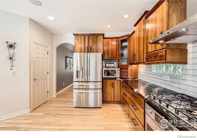 933 Xenon Ct, Golden, CO 80401 - kitchen featuring appliances with stainless steel finishes, under cabinet range hood, arched walkways, brown cabinetry, and tasteful backsplash