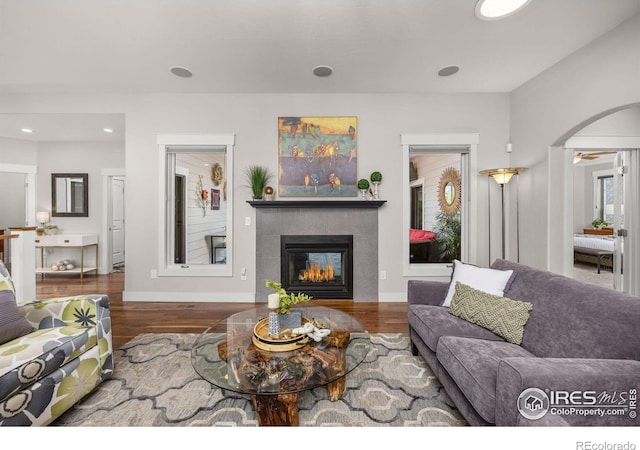living room with a glass covered fireplace, wood finished floors, recessed lighting, baseboards, and arched walkways