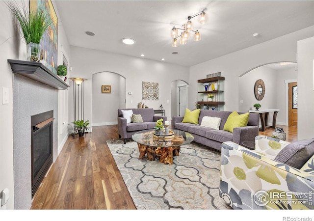 living area with arched walkways, a glass covered fireplace, wood finished floors, recessed lighting, and baseboards