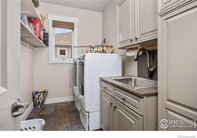 clothes washing area with washer and clothes dryer, baseboards, cabinet space, and dark stone finish flooring