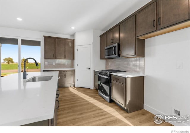 kitchen featuring stainless steel appliances, a sink, dark brown cabinetry, light wood-style flooring, and recessed lighting