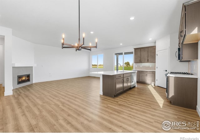 kitchen with stainless steel appliances, a sink, light countertops, a center island with sink, and backsplash