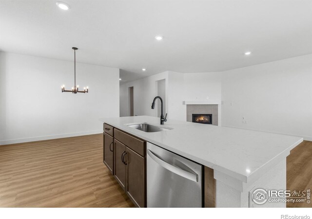 kitchen with stainless steel dishwasher, a sink, open floor plan, light wood-style flooring, and a fireplace