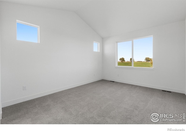 carpeted empty room featuring vaulted ceiling and baseboards