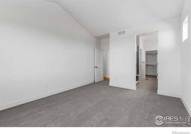 unfurnished bedroom featuring carpet floors, vaulted ceiling, baseboards, and a walk in closet