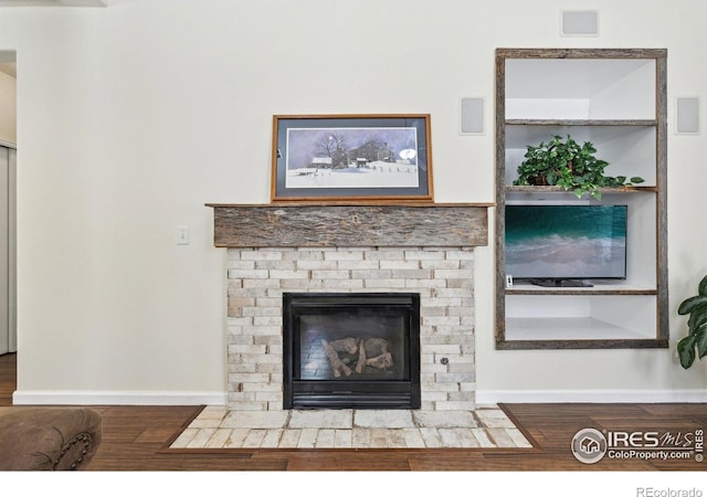 detailed view of wood finished floors, baseboards, and a brick fireplace