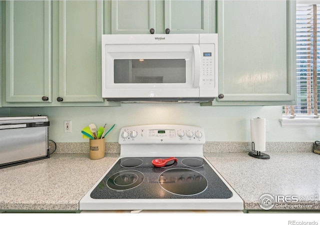 kitchen view of white appliances, green cabinets, and light countertops