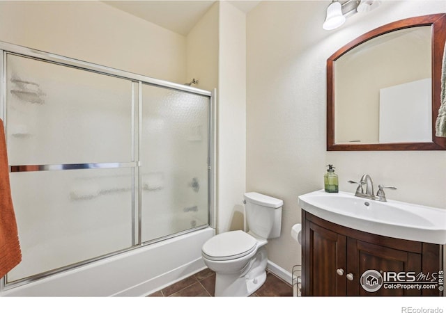bathroom featuring toilet, tile patterned floors, vanity, bath / shower combo with glass door, and baseboards
