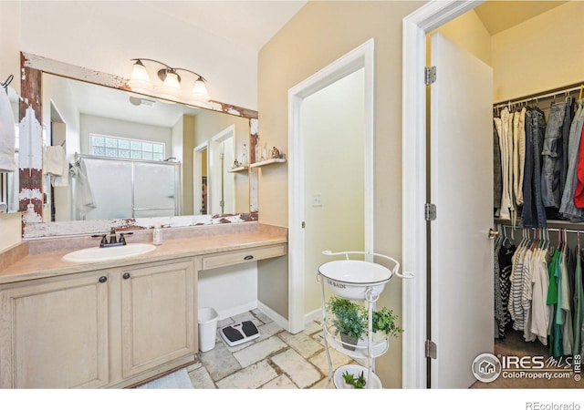 full bathroom with a walk in closet, vanity, and a shower