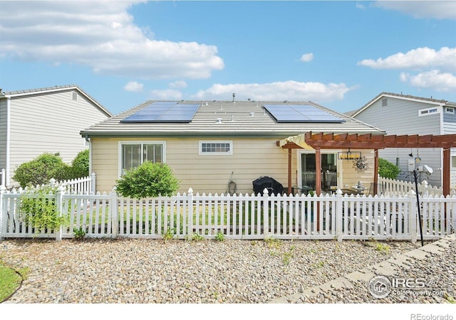 rear view of property with solar panels, a fenced front yard, and a pergola