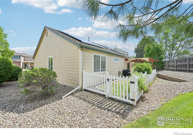 rear view of house featuring solar panels and a fenced backyard