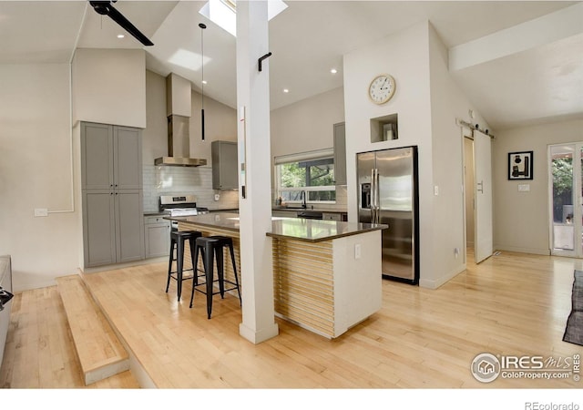 6862 Roaring Fork Trl, Boulder, CO 80301 - kitchen with stainless steel appliances, gray cabinets, high vaulted ceiling, a barn door, and wall chimney exhaust hood
