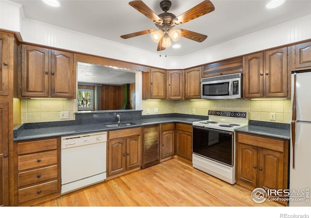 kitchen with white appliances, a sink, dark countertops, light wood-style floors, and crown molding