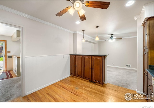 kitchen featuring a ceiling fan, a peninsula, crown molding, light wood-type flooring, and brown cabinets