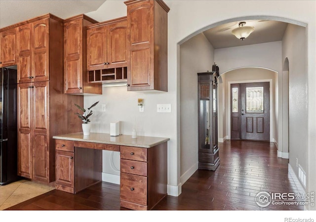 109 Veronica Dr, Windsor, CO 80550 - kitchen with dark wood-type flooring, baseboards, brown cabinetry, arched walkways, and freestanding refrigerator