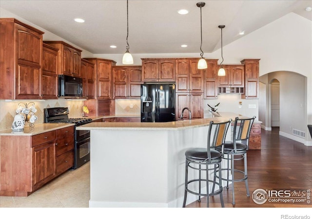 109 Veronica Dr, Windsor, CO 80550 - kitchen featuring black appliances, a spacious island, backsplash, arched walkways, and a kitchen bar