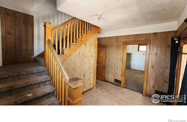 stairs with carpet flooring, wooden walls, and a textured ceiling