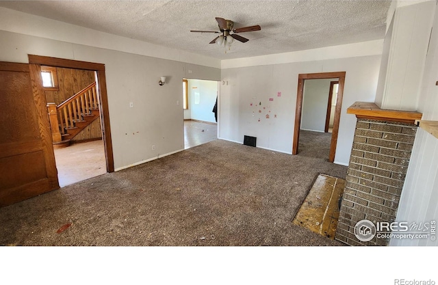 unfurnished living room with ceiling fan, stairway, carpet floors, and a textured ceiling