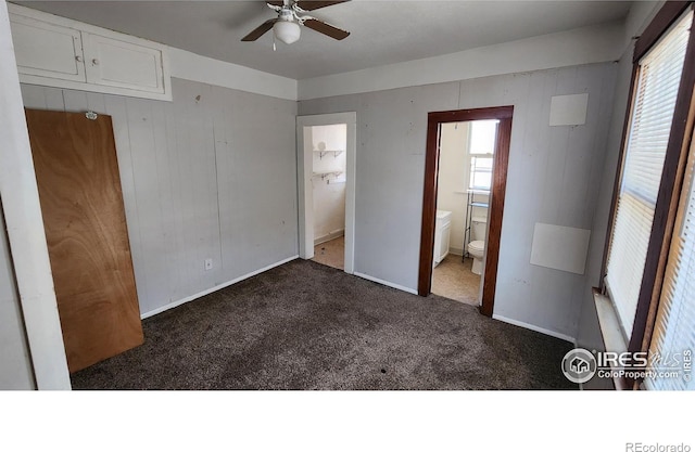 unfurnished bedroom with carpet flooring, multiple windows, ensuite bathroom, baseboards, and wooden walls
