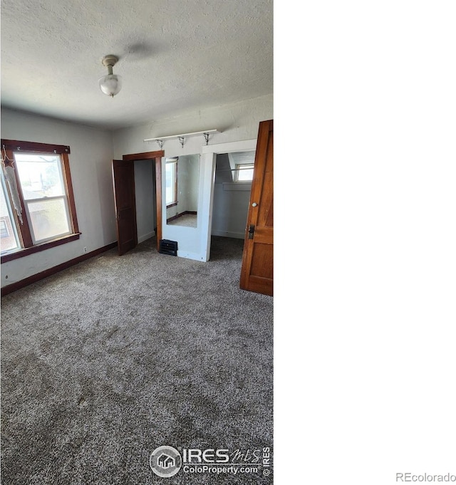 unfurnished bedroom featuring carpet, multiple windows, baseboards, and a textured ceiling