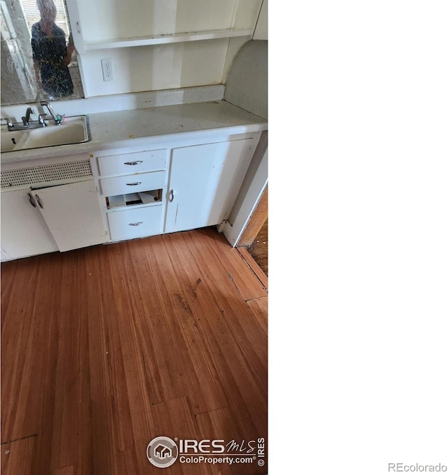 kitchen featuring white cabinets, light countertops, wood finished floors, and a sink