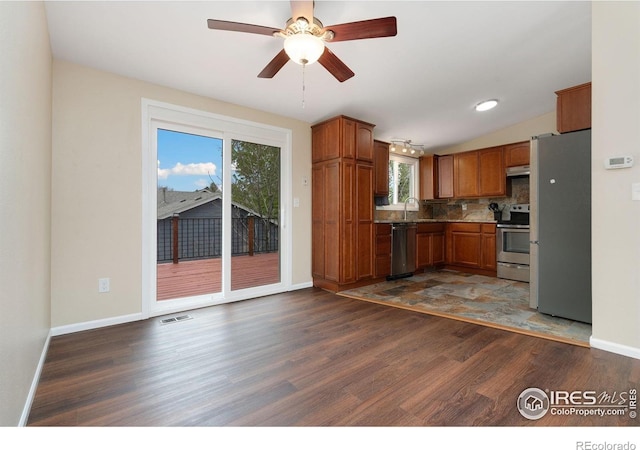 kitchen with stainless steel appliances, wood finished floors, brown cabinets, backsplash, and a sink