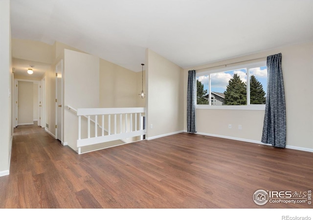 empty room featuring wood finished floors, baseboards, and vaulted ceiling