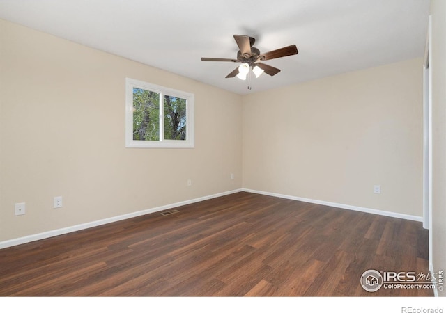 spare room featuring dark wood-style flooring, a ceiling fan, and baseboards