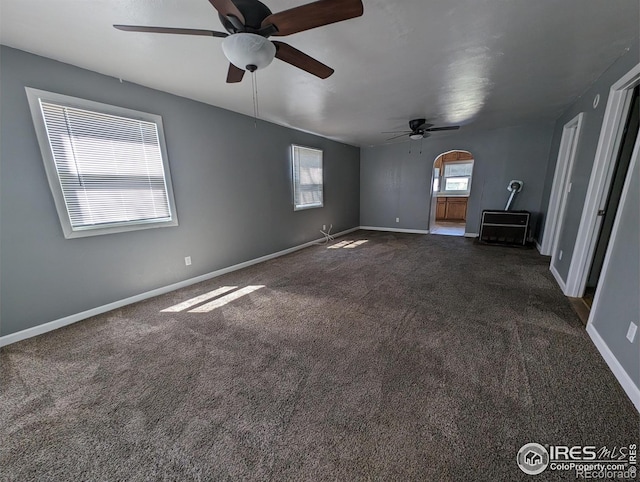 unfurnished room with a ceiling fan, dark colored carpet, and baseboards