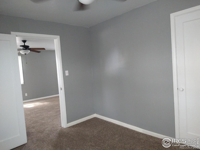 unfurnished room with a ceiling fan, dark carpet, and baseboards