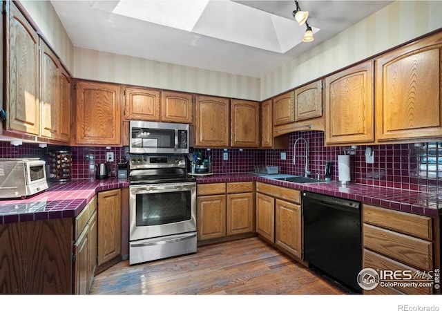 2702 W 23rd St, Greeley, CO 80634 - kitchen featuring stainless steel appliances, tile countertops, a sink, wood finished floors, and brown cabinets