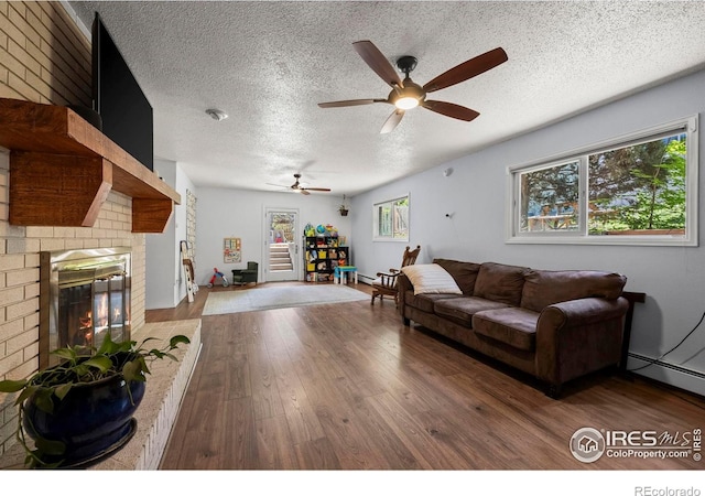 2702 W 23rd St, Greeley, CO 80634 - living area with a ceiling fan, wood-type flooring, a textured ceiling, a brick fireplace, and a baseboard heating unit