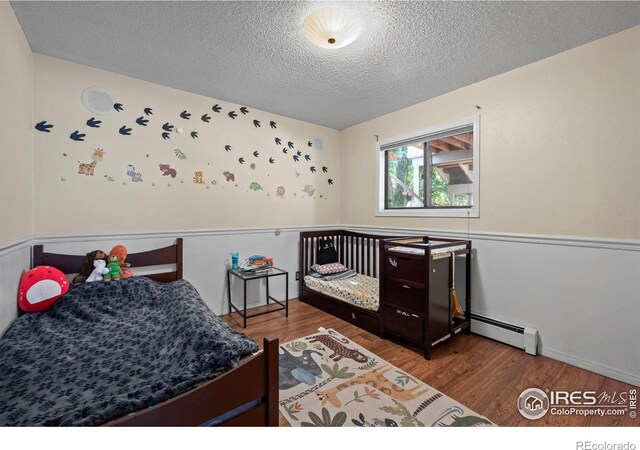 2702 W 23rd St, Greeley, CO 80634 - bedroom featuring wood finished floors, a textured ceiling, a baseboard heating unit, and baseboards