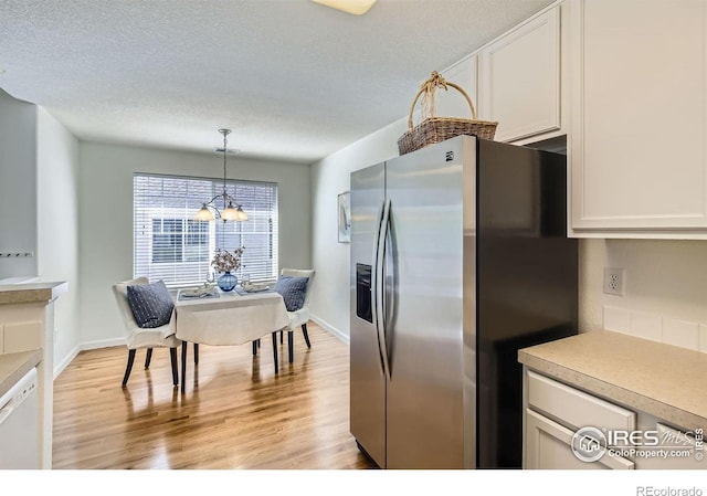 kitchen featuring stainless steel fridge with ice dispenser, light countertops, light wood finished floors, decorative light fixtures, and a textured ceiling