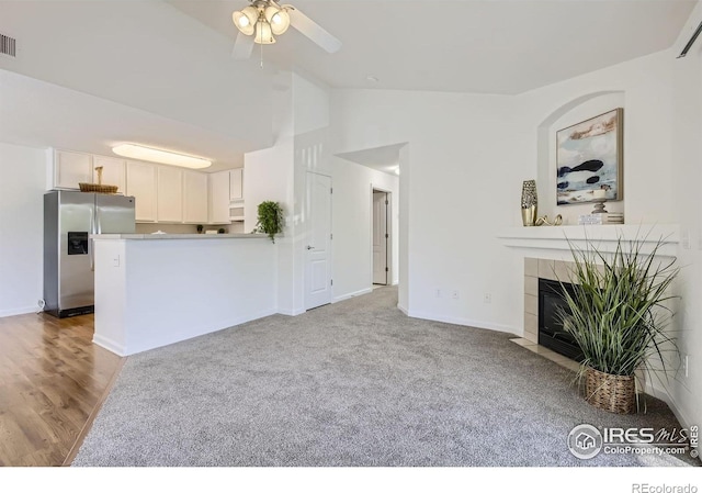 unfurnished living room with a ceiling fan, a tiled fireplace, baseboards, high vaulted ceiling, and light wood-style floors