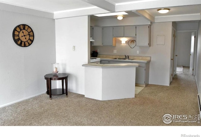 kitchen with a sink, light carpet, gray cabinets, light countertops, and a peninsula
