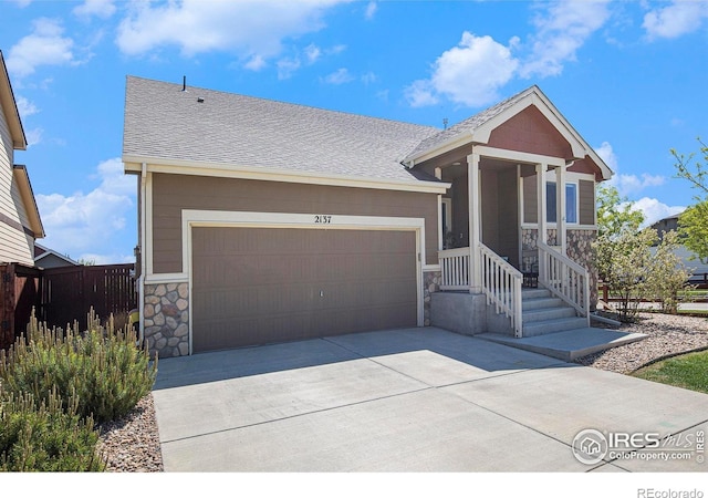 view of front of property featuring stone siding, a shingled roof, fence, and a garage