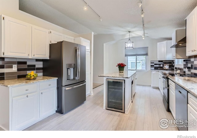 kitchen featuring stainless steel appliances, wine cooler, track lighting, wall chimney exhaust hood, and backsplash