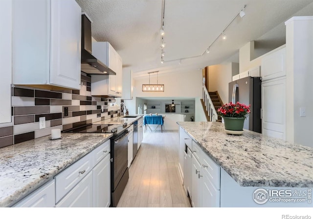 kitchen with appliances with stainless steel finishes, wall chimney range hood, a sink, white cabinetry, and light wood finished floors