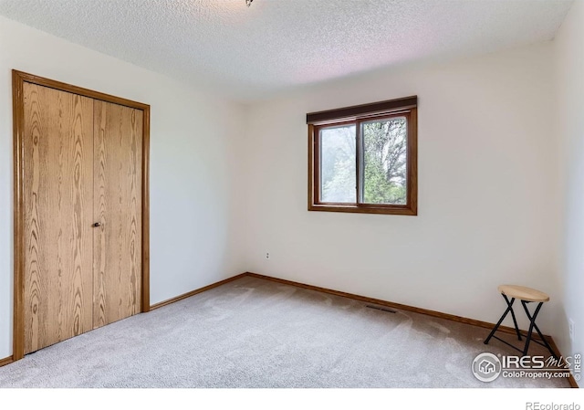 unfurnished bedroom with carpet floors, a textured ceiling, baseboards, and a closet