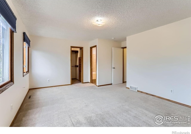 unfurnished bedroom with a textured ceiling, light colored carpet, baseboards, and a walk in closet