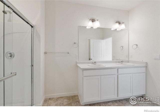 full bath featuring a shower stall, double vanity, and baseboards