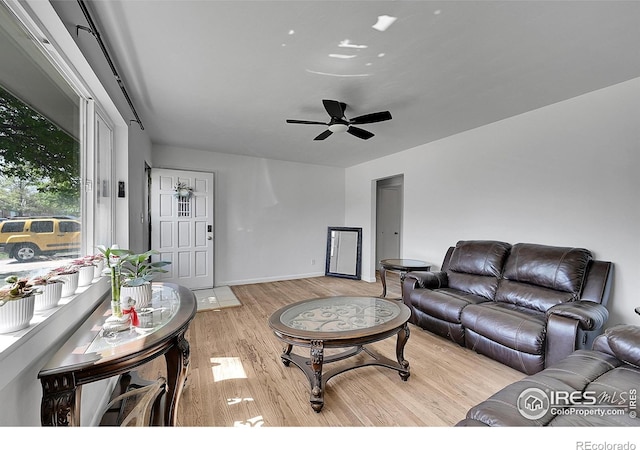 living area with light wood-style floors, a ceiling fan, and baseboards
