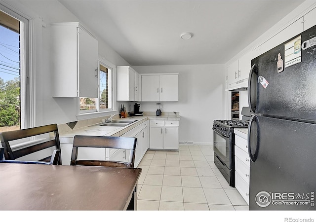 kitchen featuring black appliances, under cabinet range hood, light tile patterned flooring, white cabinetry, and a sink