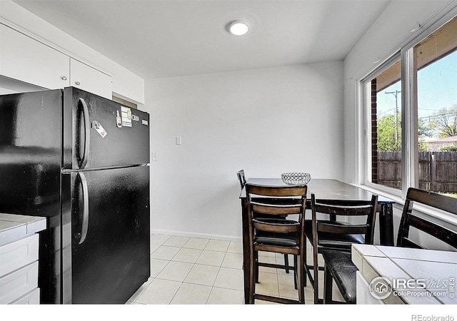 kitchen featuring freestanding refrigerator, white cabinets, light tile patterned floors, baseboards, and tile counters