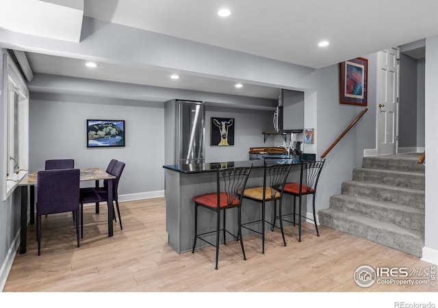 kitchen with a kitchen bar, light wood finished floors, baseboards, a peninsula, and recessed lighting
