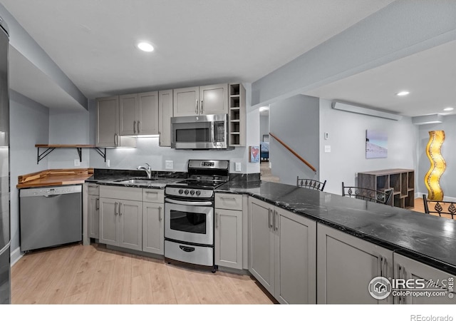 kitchen with appliances with stainless steel finishes, open shelves, a sink, light wood-type flooring, and gray cabinets